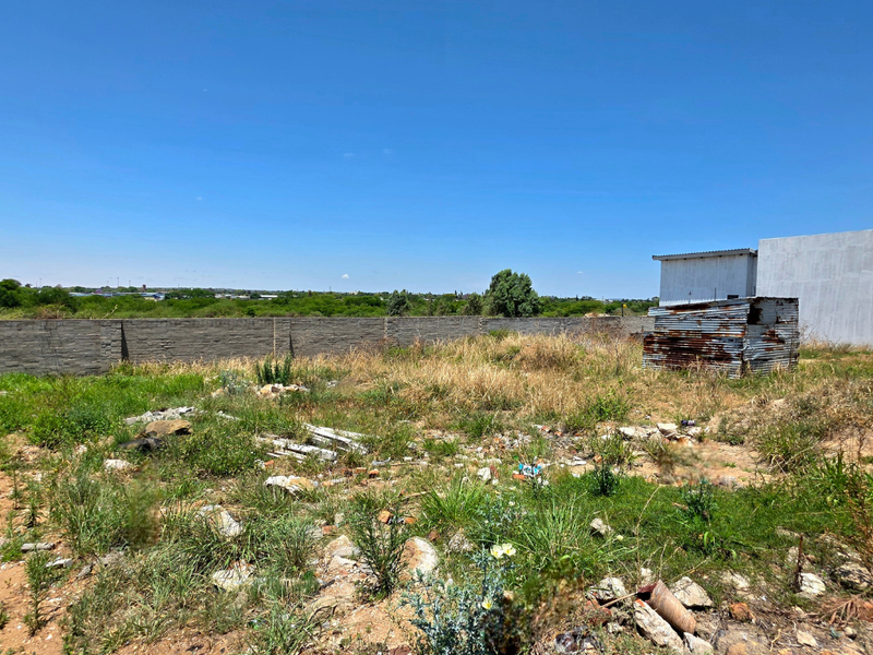 Vacant residential land featuring a perimeter brick wall and a small, weathered corrugated metal structure on the property.