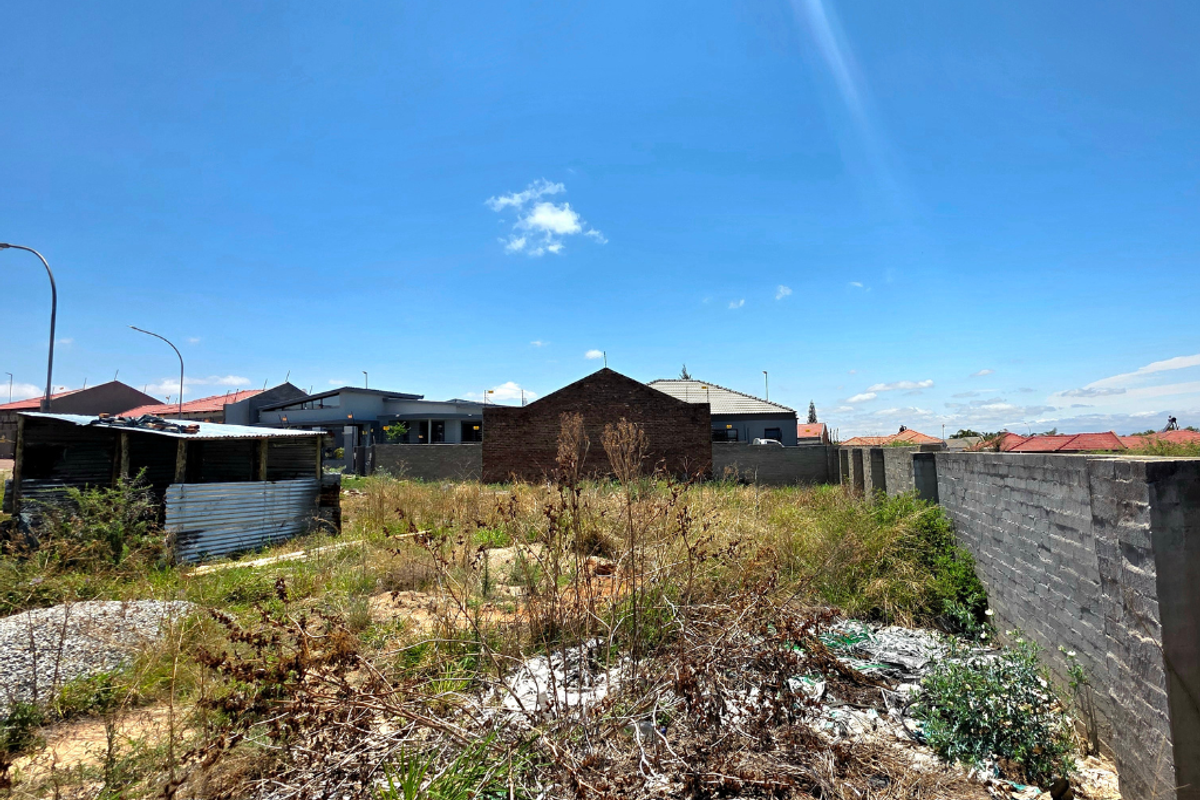 Vacant residential land featuring a perimeter brick wall and a small corrugated metal structure, requiring clearing and site preparation.