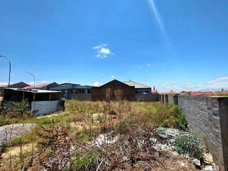 Vacant residential land featuring a perimeter brick wall and a small corrugated metal structure, requiring clearing and site preparation.