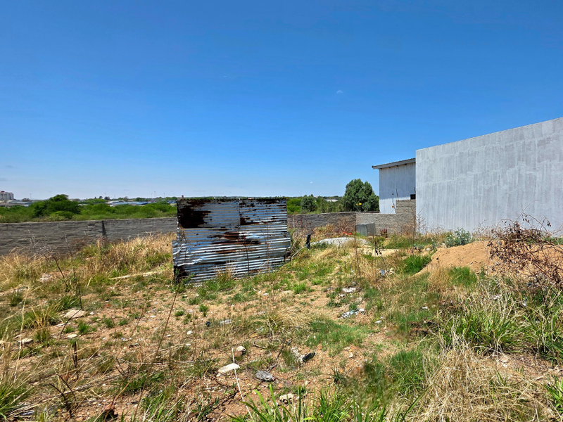 A vacant residential plot featuring a boundary wall and a dilapidated corrugated metal structure, requiring significant site clearing and development.