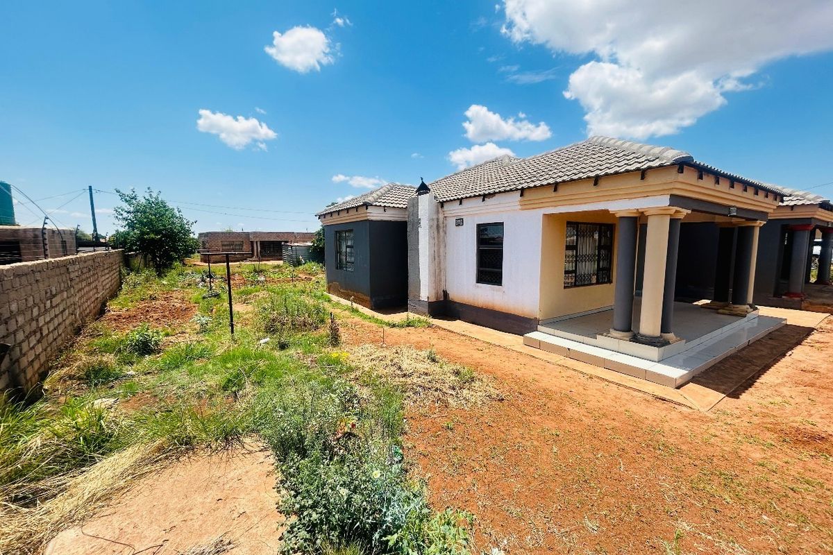 Rear view of the house featuring a covered patio with concrete columns, security bars on windows, and an expansive, unlandscaped garden area.