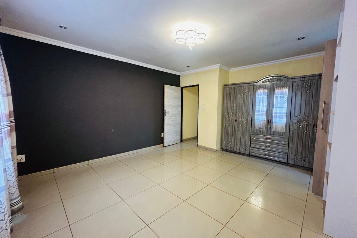 A bedroom featuring tiled flooring, recessed ceiling lighting, and a large built-in wardrobe with a contrasting dark feature wall.