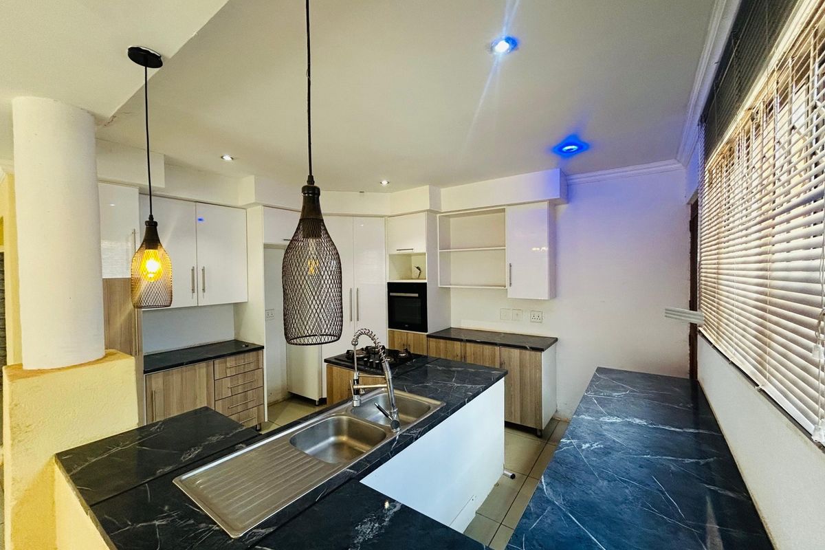 Modern kitchen featuring marble-look countertops, built-in oven, gas hob, and ample cabinetry, illuminated by stylish pendant lights and recessed ceiling lighting.