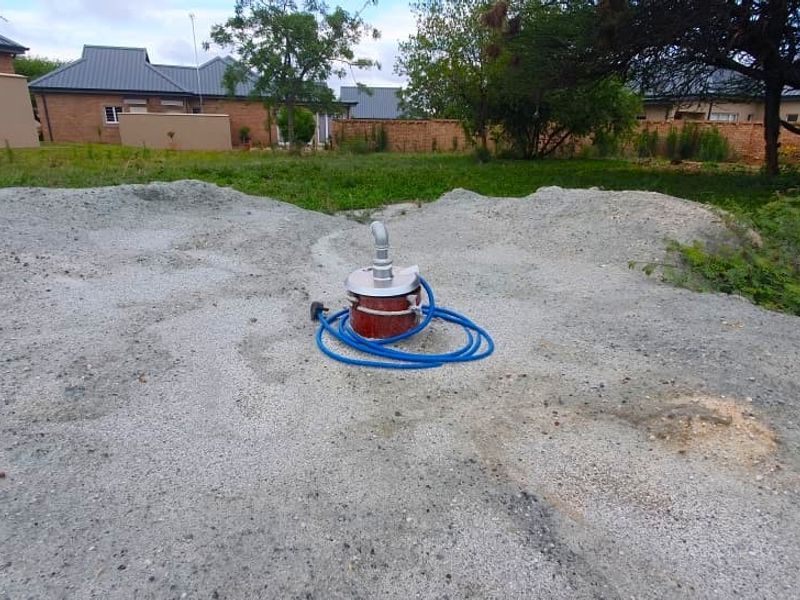 A vacant residential plot featuring a borehole pump installation set within a grassy area with surrounding perimeter walls.