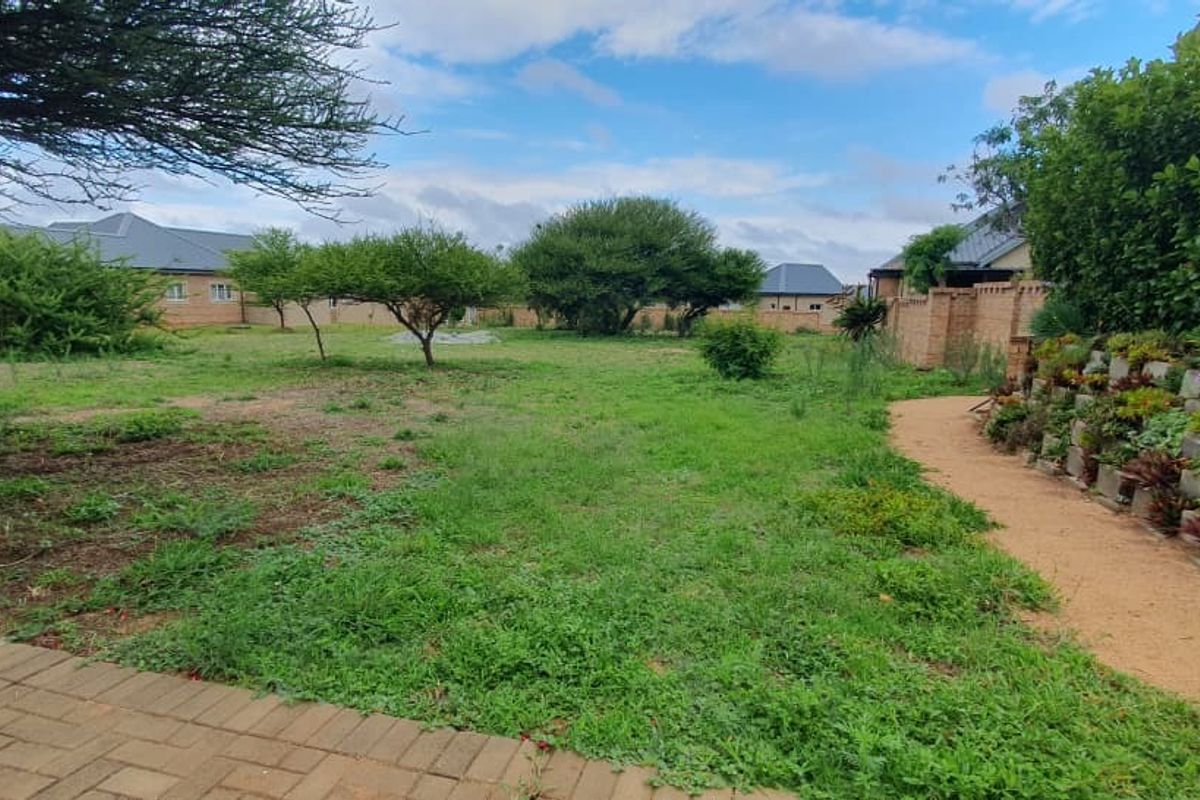 A spacious residential garden featuring a paved patio, a tiered brick retaining wall with established plantings, and a perimeter boundary wall.