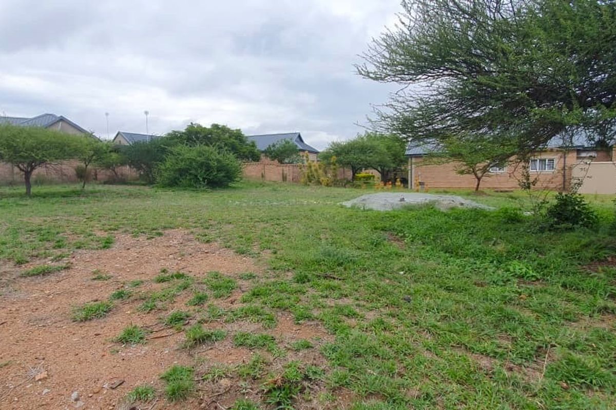 A view of a vacant residential plot featuring established trees, grassed terrain, and surrounding boundary walls.