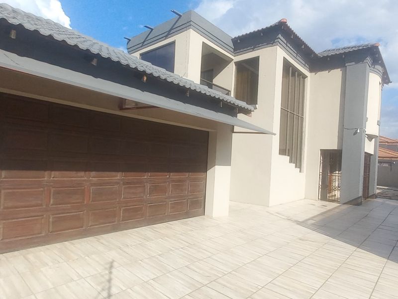 Modern double-storey residential facade featuring a large wooden garage door, tiled driveway, and secure perimeter electric fencing.
