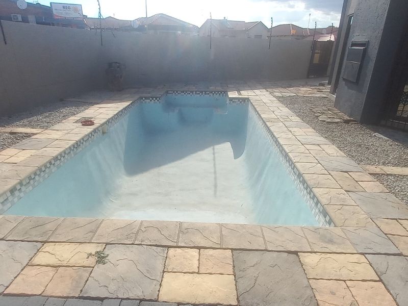 Outdoor pool area featuring a paved surround and perimeter wall, currently empty and requiring maintenance or landscaping to enhance the exterior space.