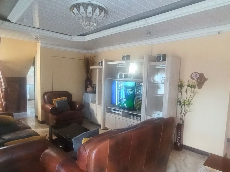 A living room area featuring tiled flooring, decorative ceiling molding, and an adjacent staircase leading to the upper level.