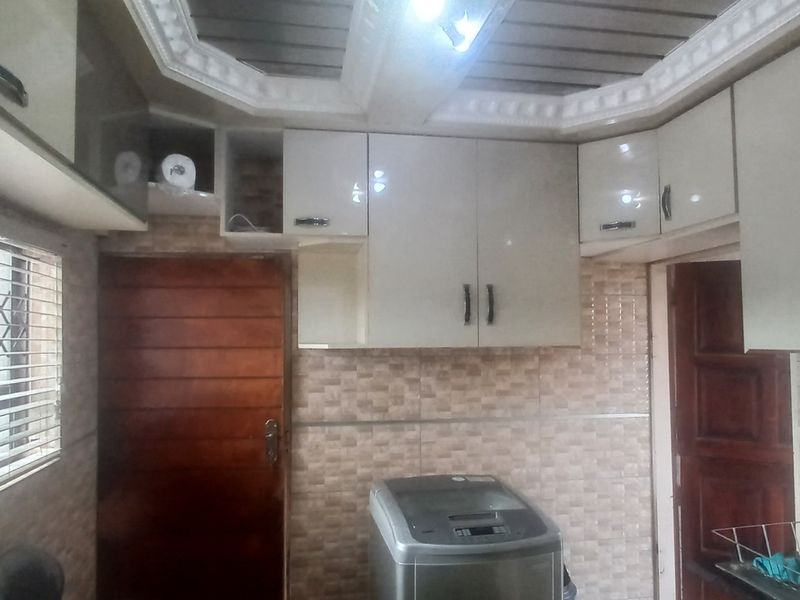 A functional kitchen area featuring built-in cabinetry, tiled backsplash, and a security gate on the window.