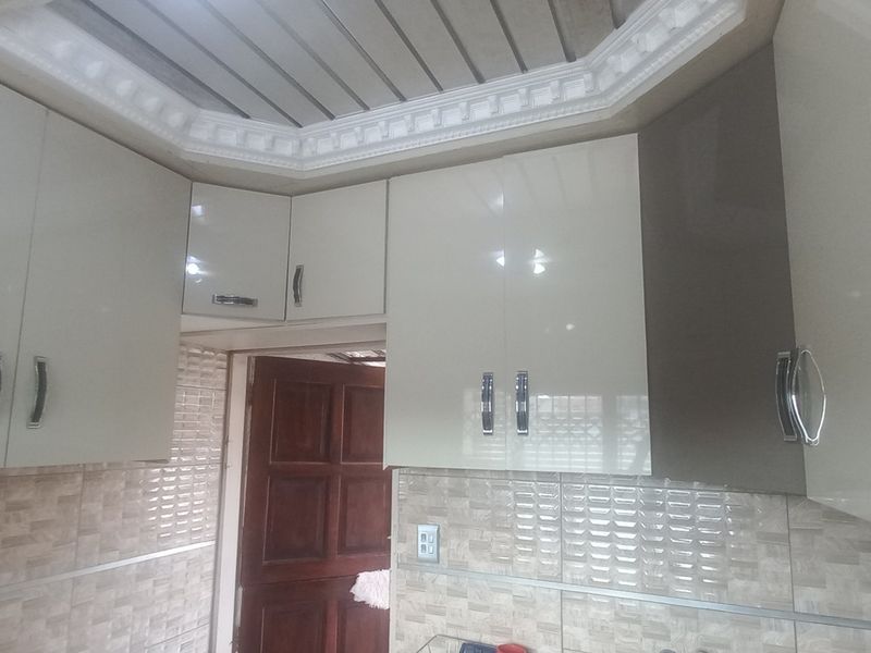 A kitchen area featuring modern high-gloss cabinetry, a tiled backsplash, and decorative ceiling molding, providing a clean and functional storage space.