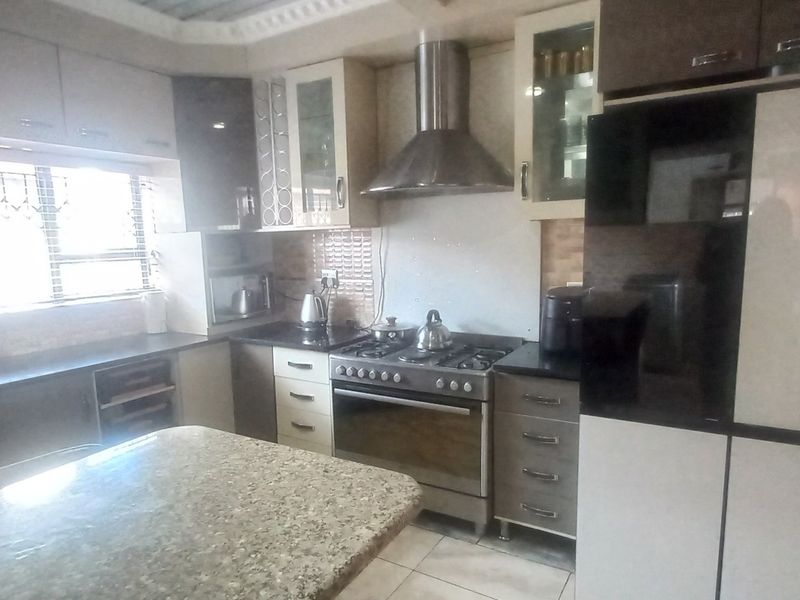 A functional kitchen featuring granite countertops, built-in cabinetry, a stainless steel extractor fan, and a gas stove with an oven.