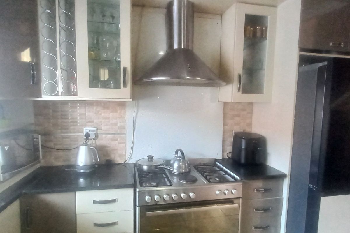 A functional kitchen featuring built-in cabinetry, granite countertops, a tiled backsplash, and a stainless steel gas stove with an integrated extractor fan.