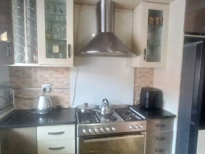 A functional kitchen featuring built-in cabinetry, granite countertops, a tiled backsplash, and a stainless steel gas stove with an integrated extractor fan.