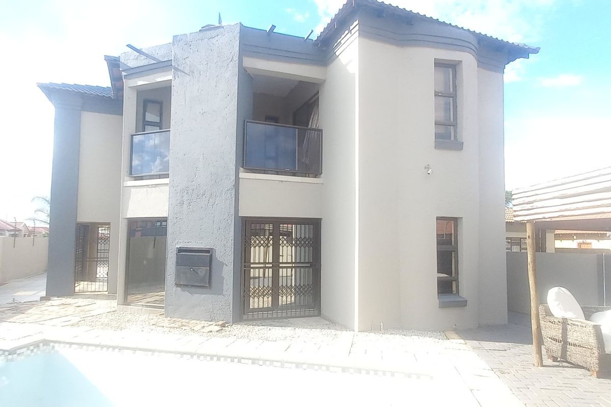 Rear view of a double-story house featuring a swimming pool, paved patio area, and balcony access.