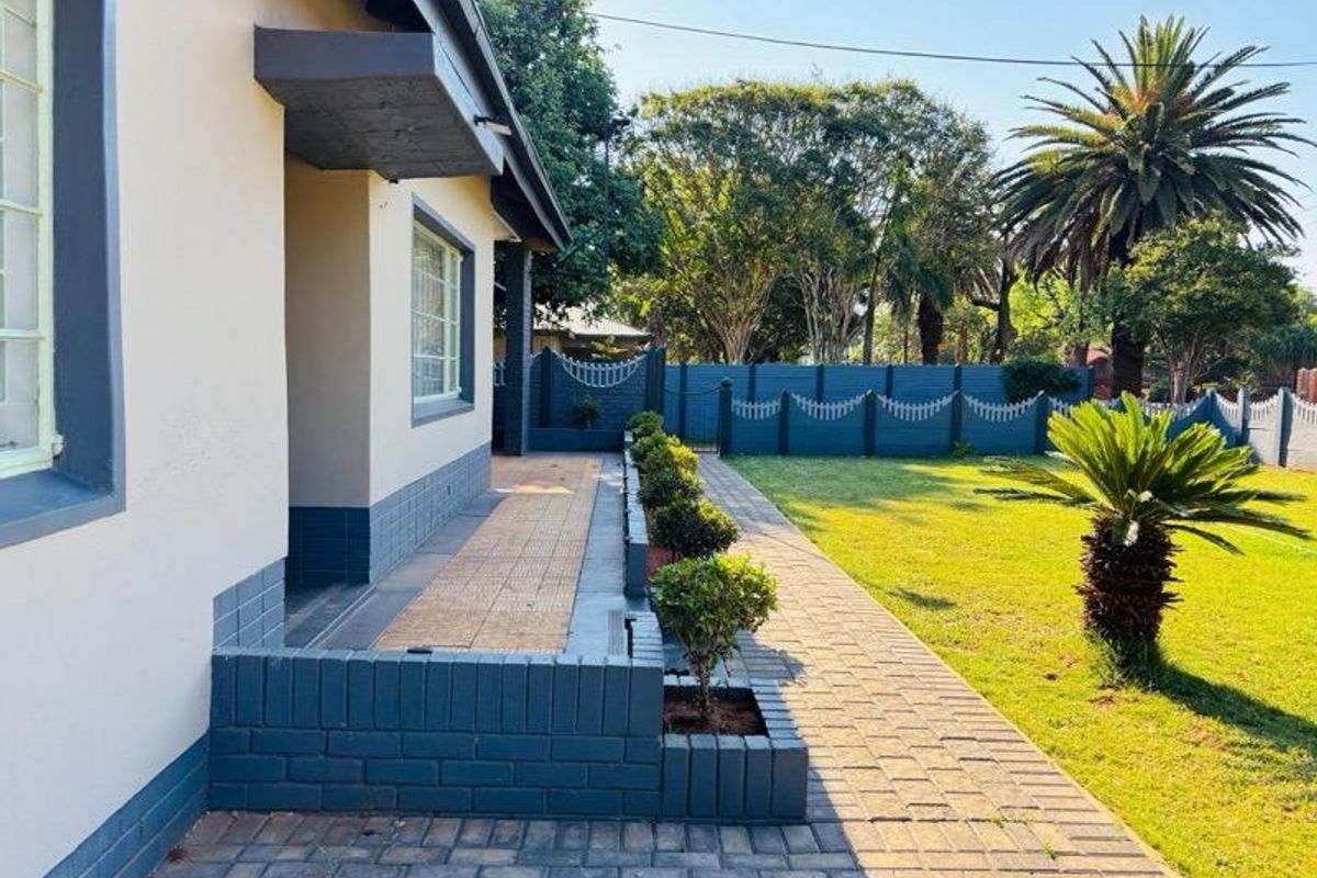 A well-maintained rear exterior featuring a paved walkway, brick planter boxes, and a secure perimeter wall bordering a landscaped garden.