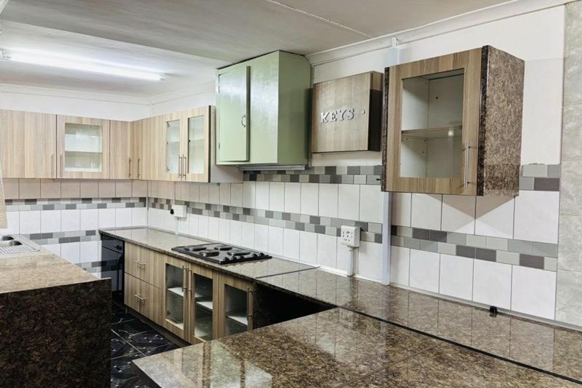 A functional kitchen featuring granite countertops, a built-in hob, and a mix of wood-grain and painted cabinetry with a tiled backsplash.