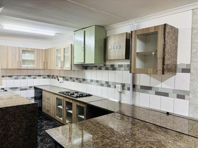 A functional kitchen featuring granite countertops, a built-in hob, and a mix of wood-grain and painted cabinetry with a tiled backsplash.