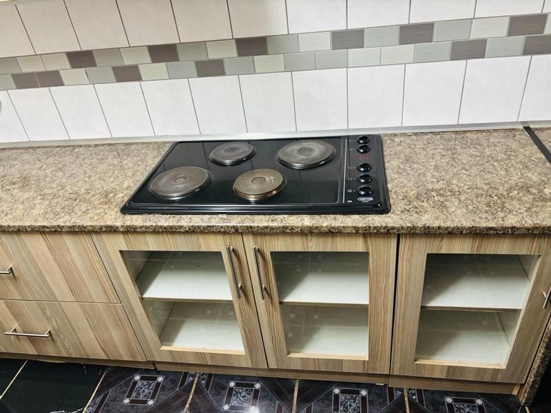A clean kitchen workspace featuring a built-in electric hob, laminate cabinetry, and a tiled backsplash with a granite-look countertop.