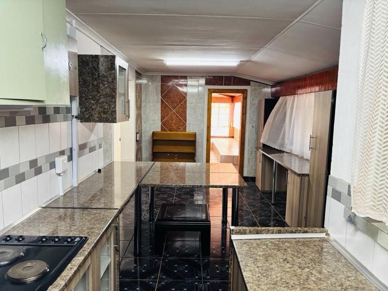 A functional kitchen featuring granite countertops, built-in cabinetry, and an electric hob, with tiled flooring and backsplash throughout the workspace.