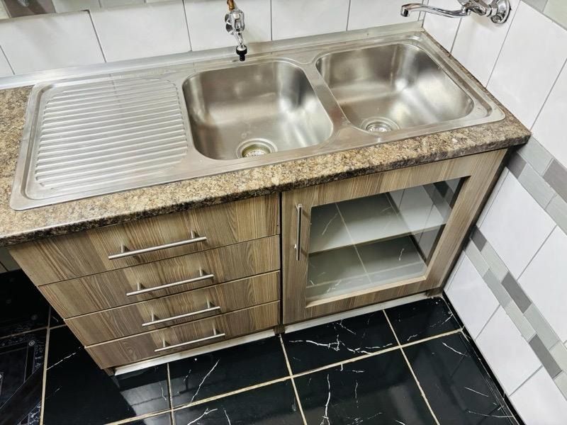 A functional scullery area featuring a double stainless steel sink, laminate countertop, and built-in cabinetry with tiled finishes.