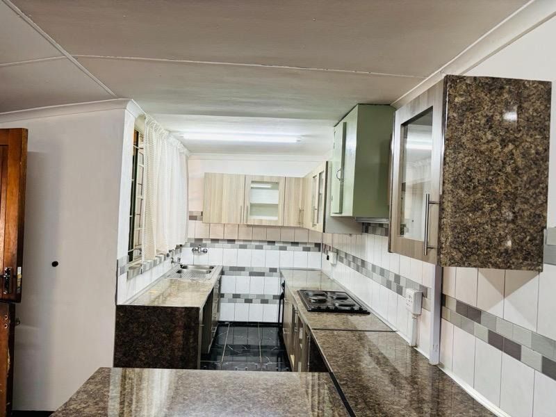 A functional kitchen featuring granite countertops, a built-in hob, stainless steel sink, and a mix of upper and lower cabinetry with tiled finishes.