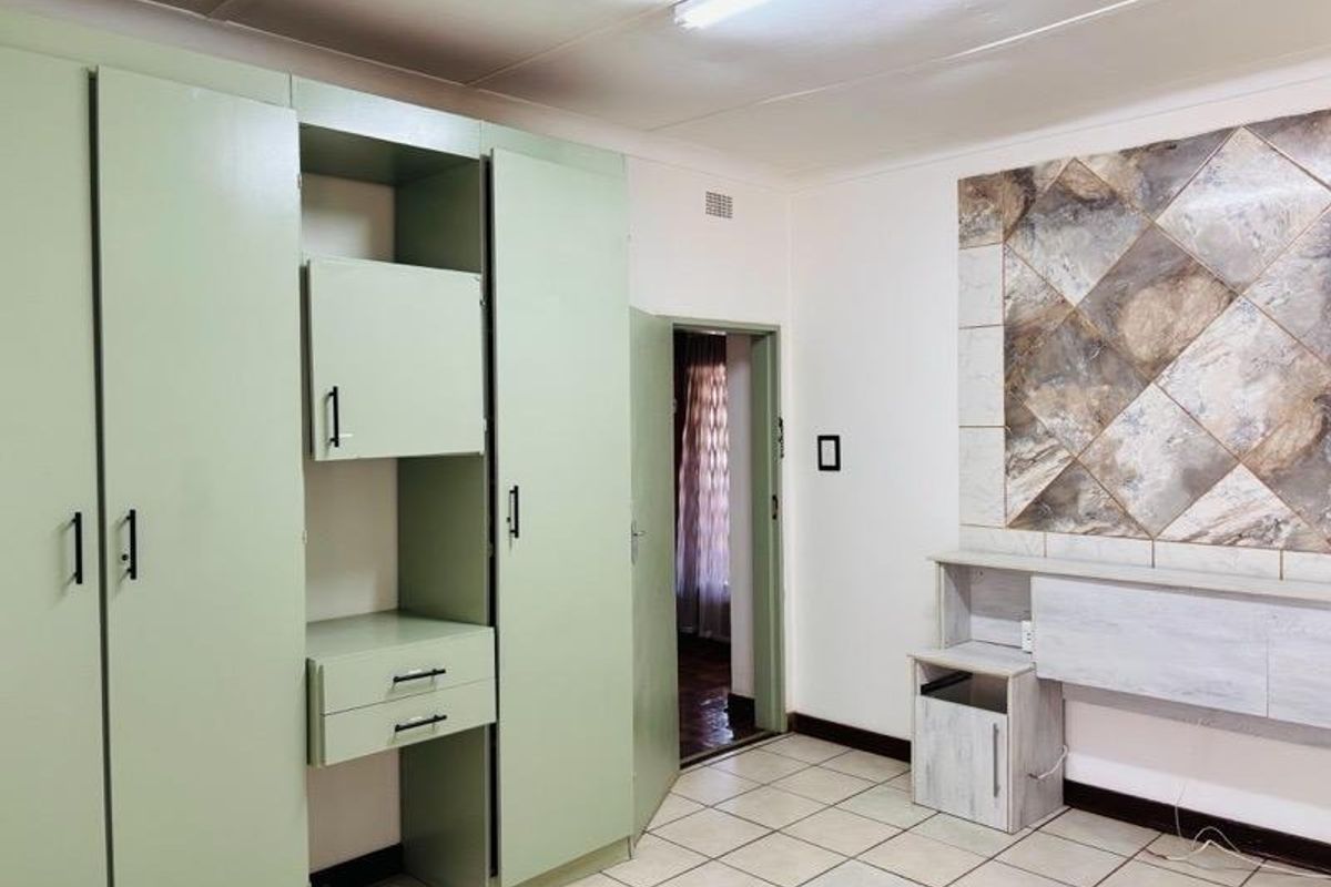 A bedroom featuring built-in cupboards, tiled flooring, and a decorative tiled wall feature, offering a functional space ready for modernization.