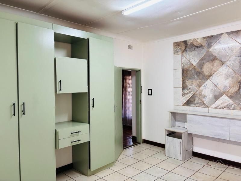 A bedroom featuring built-in cupboards, tiled flooring, and a decorative tiled wall feature, offering a functional space ready for modernization.