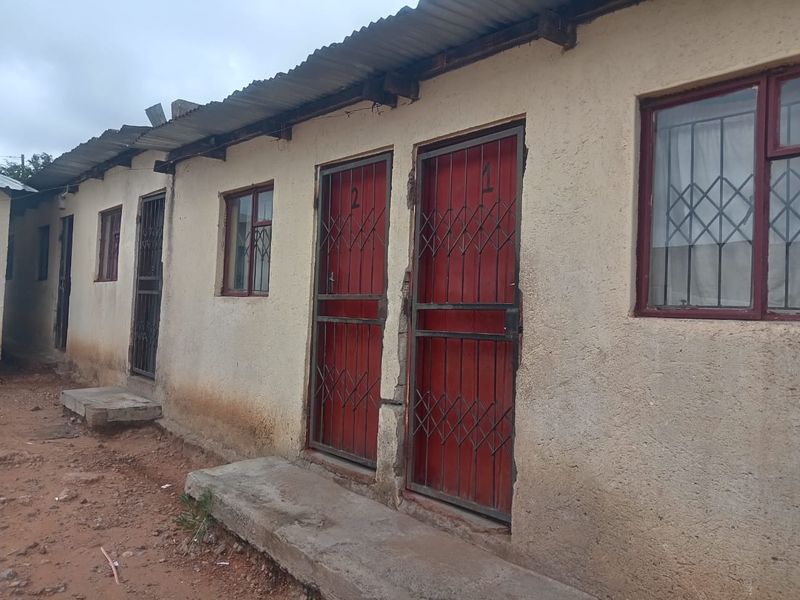 Exterior view of a row of residential units featuring corrugated metal roofing, security gates, and steel window frames with visible wear to the exterior walls.