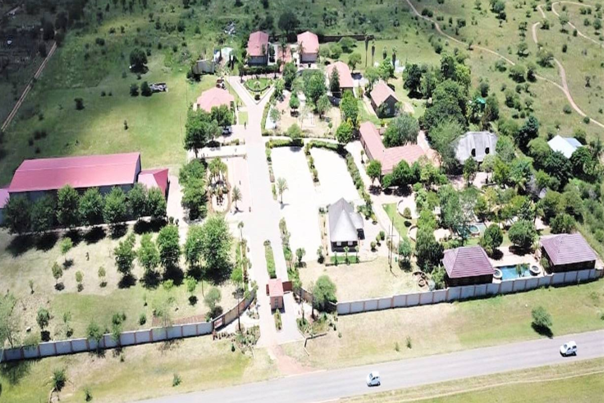 An aerial view of a large small holding property featuring multiple buildings, a swimming pool, extensive landscaped grounds, and a paved driveway.