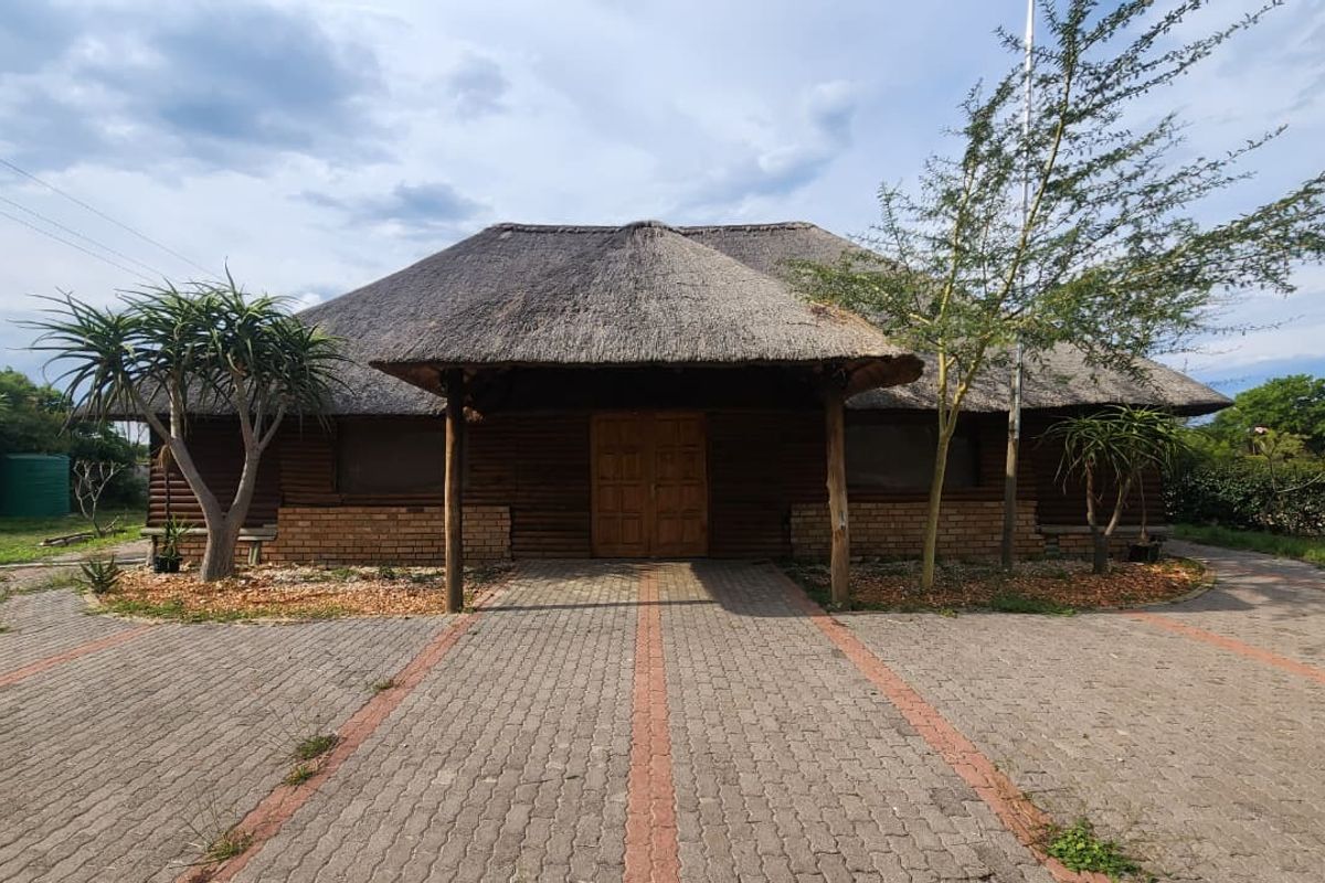 Front elevation of a rustic thatch-roofed dwelling featuring a paved driveway and covered entrance porch.
