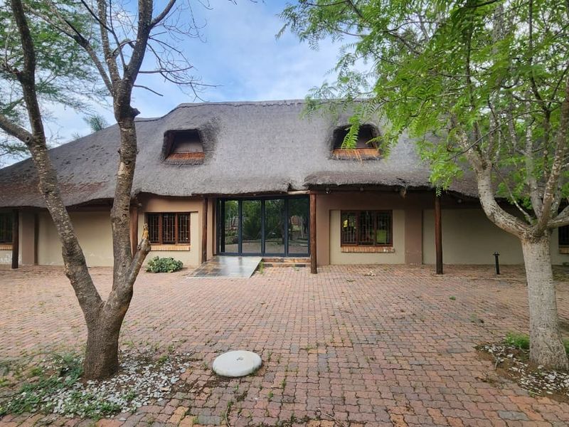 Front elevation of a traditional thatched-roof small holding featuring a large brick-paved courtyard and established trees.
