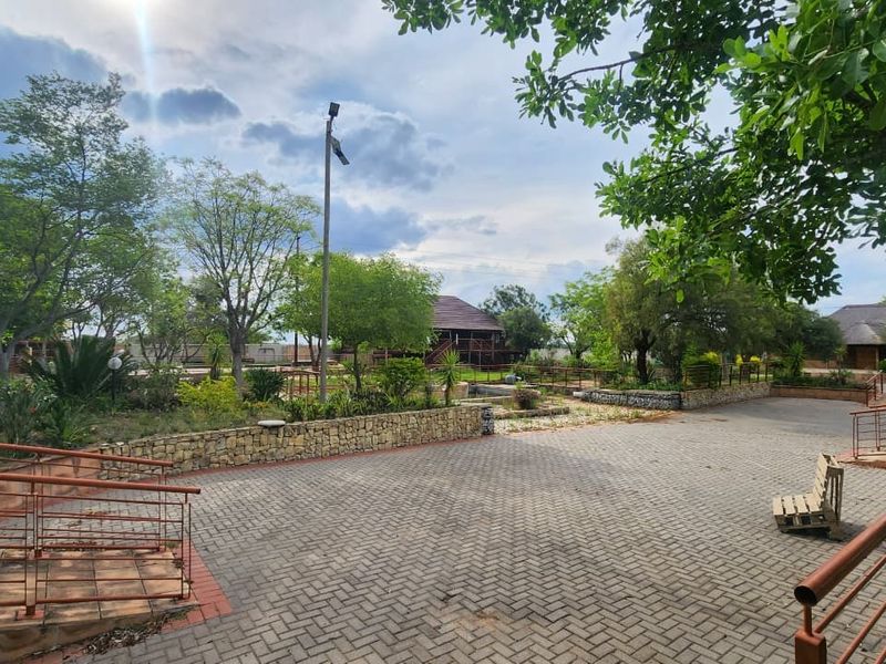 Spacious outdoor area featuring paved surfaces, stone retaining walls, and established garden landscaping with metal safety railings.