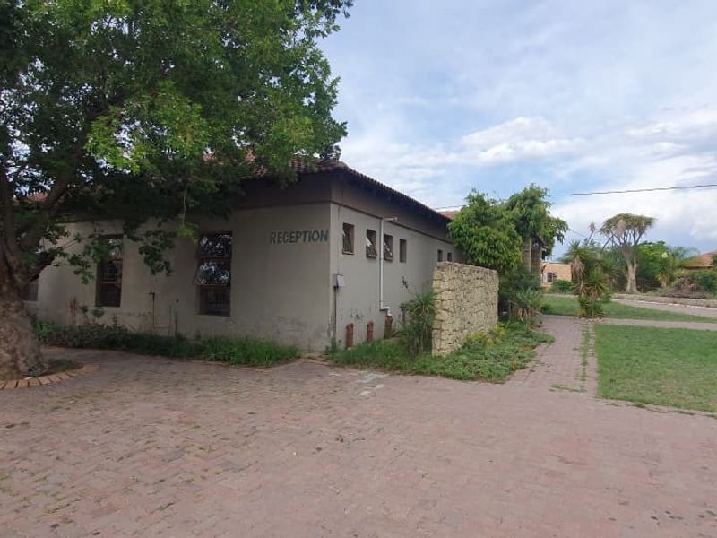 Exterior view of the property reception area featuring a paved driveway, stone feature wall, and established trees on the small holding.
