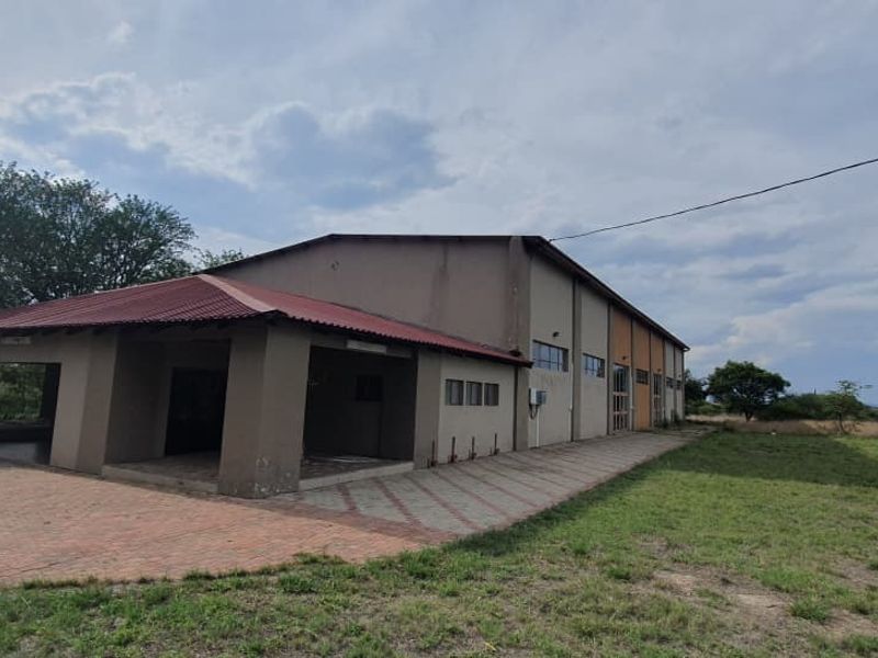 Rear view of a large industrial-style building featuring a covered patio area, corrugated metal roofing, and extensive paved surroundings on a small holding.