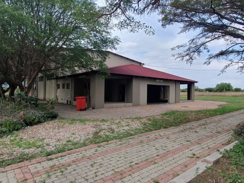 Front view of the property featuring a covered patio area, paved driveway, and established garden surroundings on a small holding.