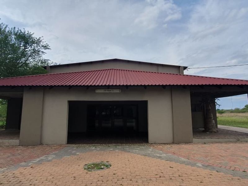 Front elevation of a small holding property featuring a covered patio area, corrugated metal roofing, and a paved driveway entrance.