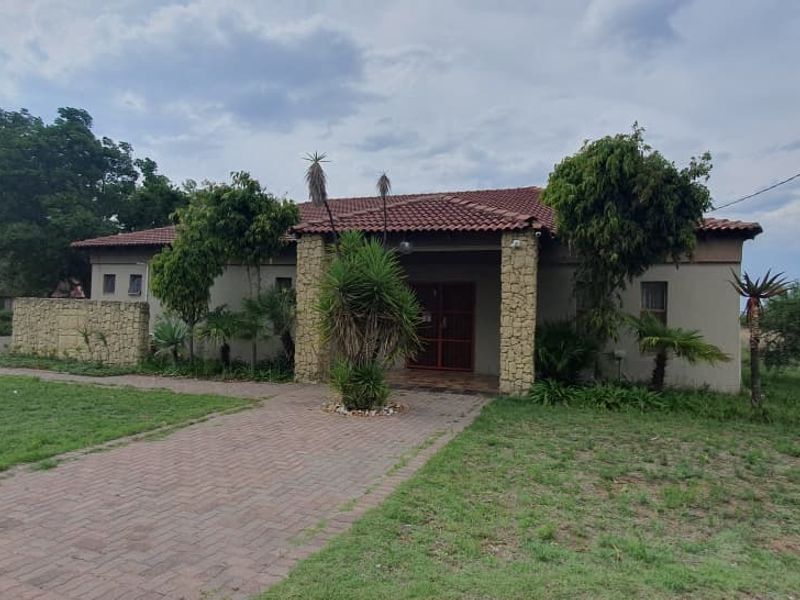 Front elevation of a small holding property featuring a tiled roof, stone-clad entrance pillars, and a paved driveway set within a spacious garden.