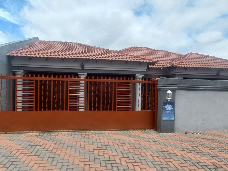 Front view of a residential property featuring a tiled roof, secure perimeter wall with a sliding gate, and a paved driveway.