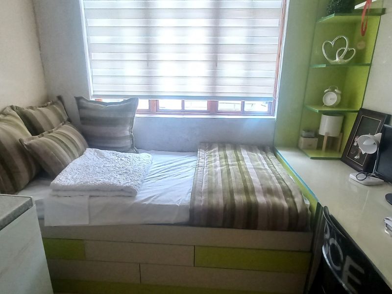 A compact bedroom featuring a built-in bed base with integrated storage, a fitted desk, and custom shelving units.