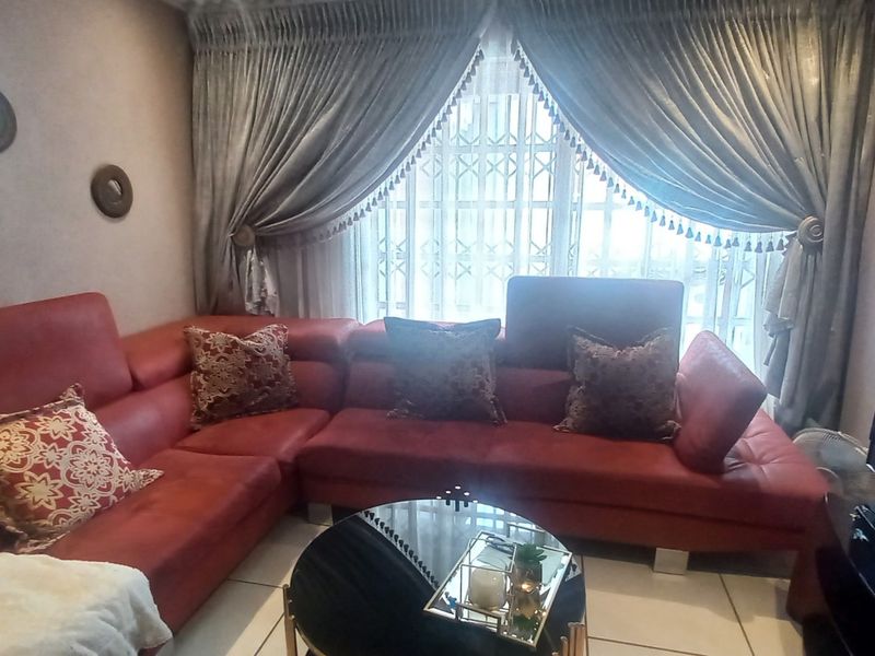 A cozy living room featuring tiled flooring and a window fitted with a security gate and decorative curtains.