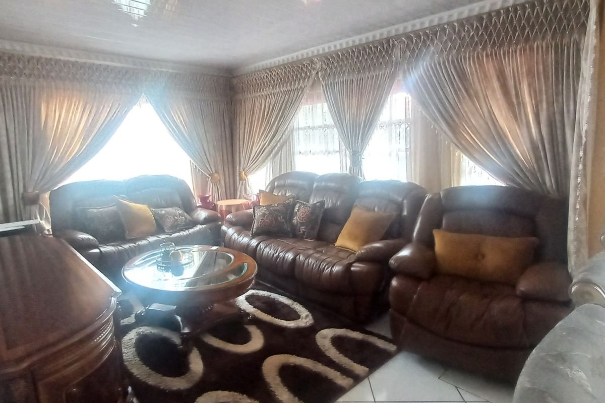 A spacious living room featuring tiled flooring, ceiling coving, and large windows that allow for ample natural light.