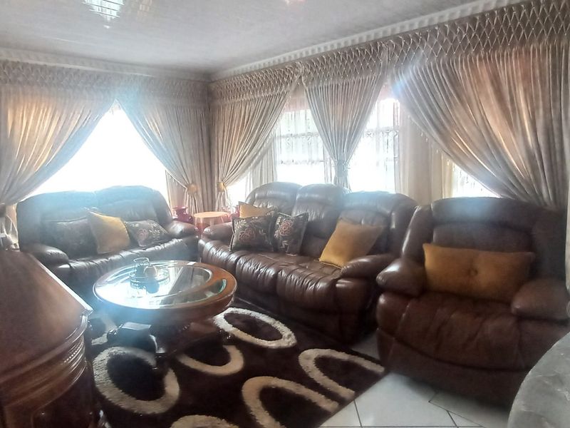 A spacious living room featuring tiled flooring, ceiling coving, and large windows that allow for ample natural light.