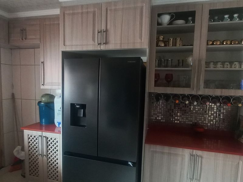A kitchen area featuring wood-finish cabinetry, glass-fronted display units, tiled backsplash, and red countertops, providing functional storage and workspace.