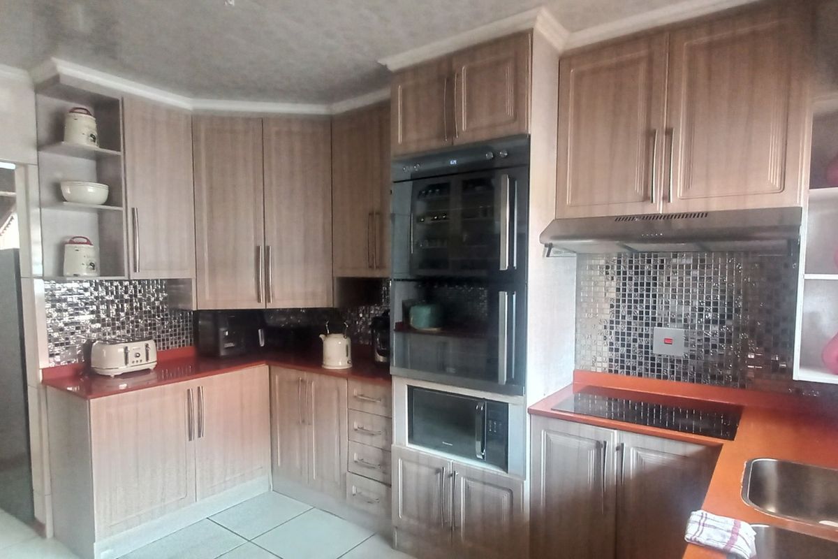 A functional kitchen featuring wood-finish cabinetry, mosaic tile backsplashes, integrated appliances, and a double sink with ample counter space.