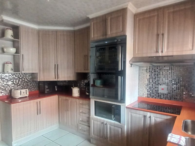 A functional kitchen featuring wood-finish cabinetry, mosaic tile backsplashes, integrated appliances, and a double sink with ample counter space.