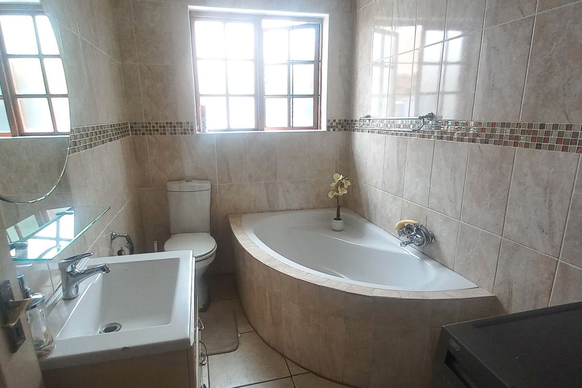 A functional bathroom featuring a corner bathtub, vanity basin, toilet, and neutral tiled finishes throughout.