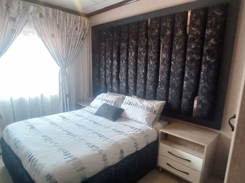 A bedroom featuring a large built-in upholstered headboard and tiled flooring, offering a functional space with neutral finishes.