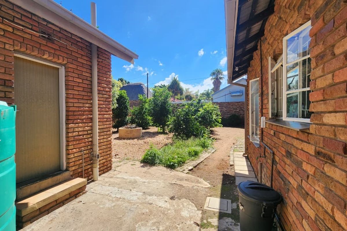 A view of the rear exterior area featuring exposed brick walls, a water storage tank, and a paved pathway leading to the garden.