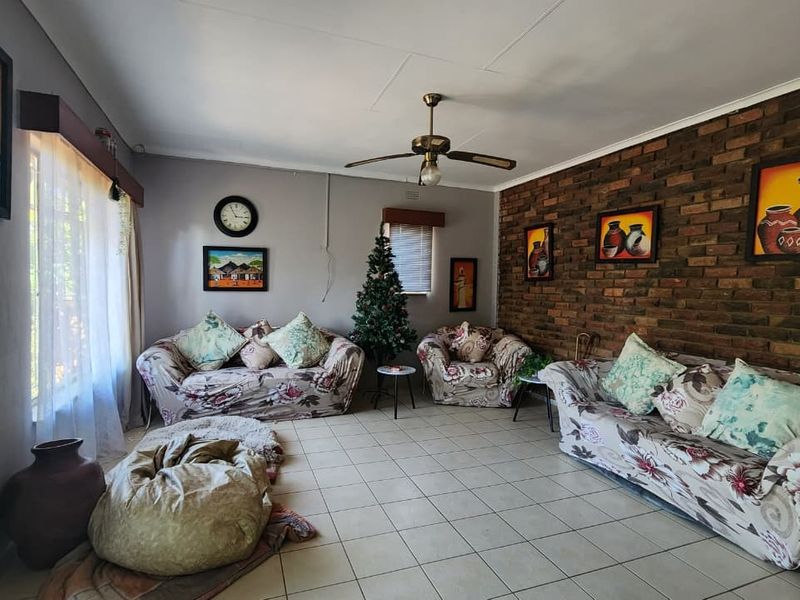 Spacious living room featuring a rustic exposed brick feature wall, tiled flooring, and a central ceiling fan.